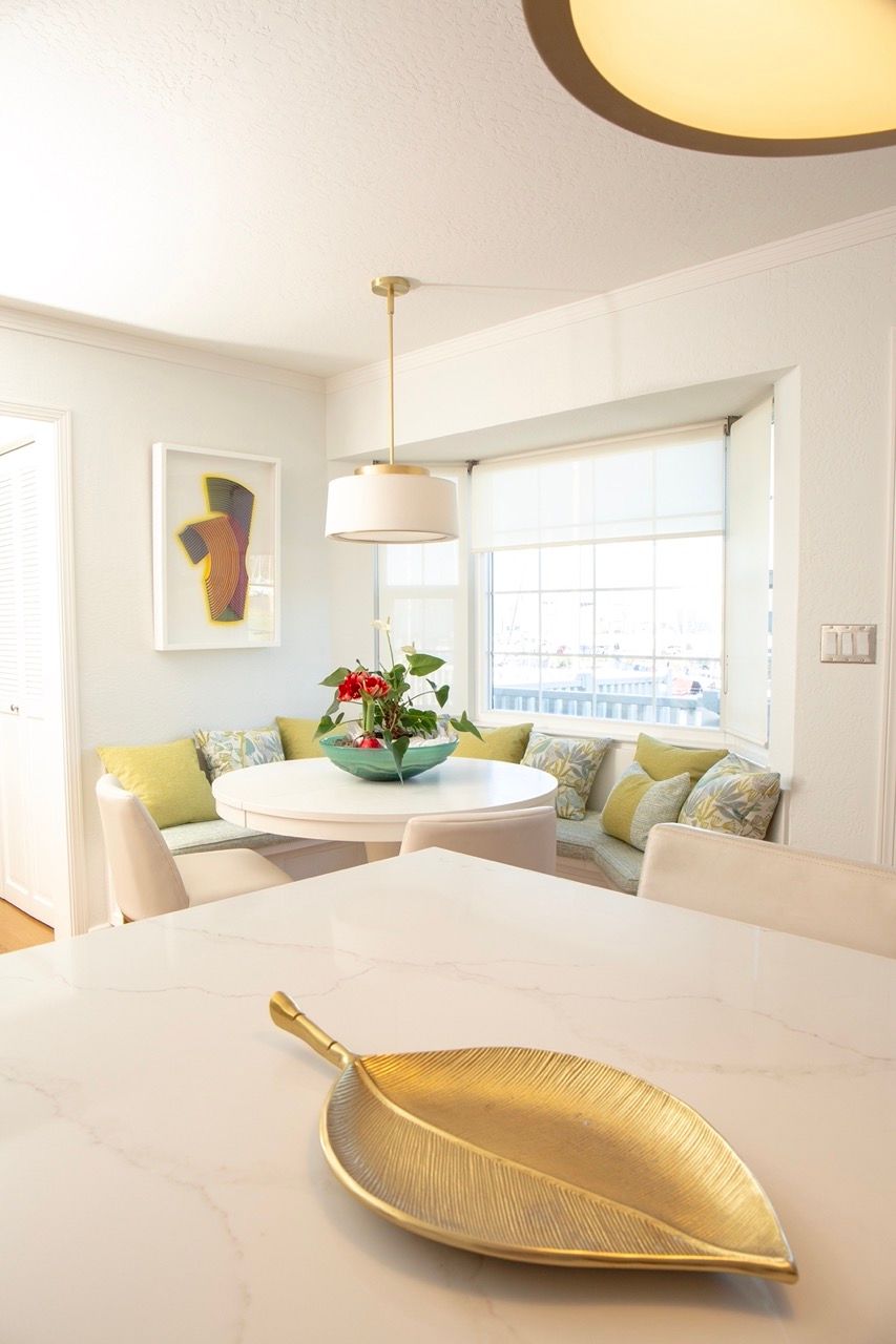 Bright dining area with white chairs, a round table, flowers, and a gold leaf dish on a counter