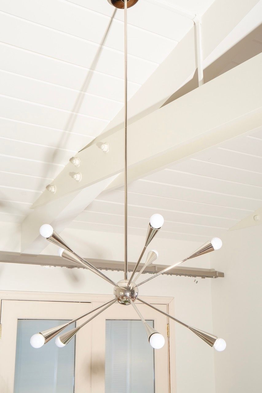 Modern chandelier with multiple arms and white globe bulbs hanging from a vaulted white ceiling
