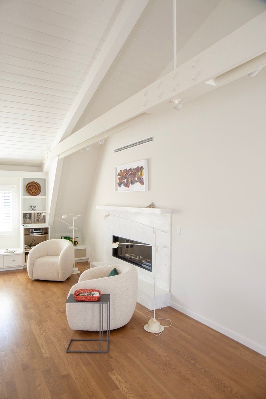 Bright living room with white walls, wood floor, fireplace, and two cream chairs by a window.