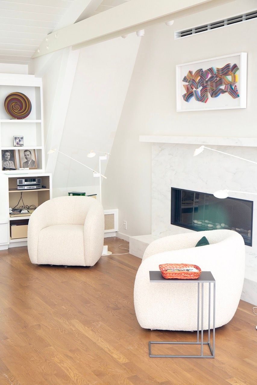 Bright living room with white chairs, wood floor, wall art, and a black fireplace