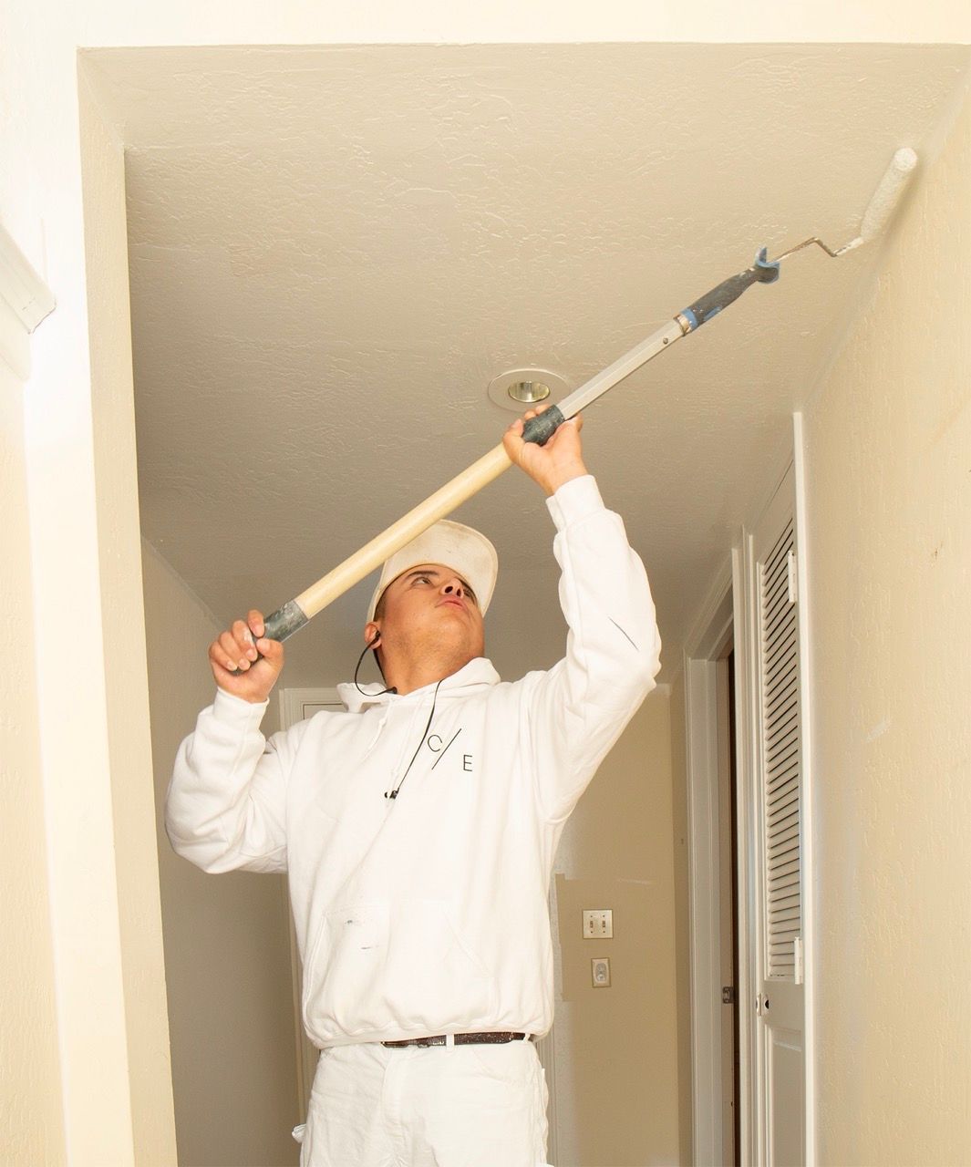 Chad Feagley of Cutting Edge Painters  painting a ceiling with a long-handled roller in a hallway