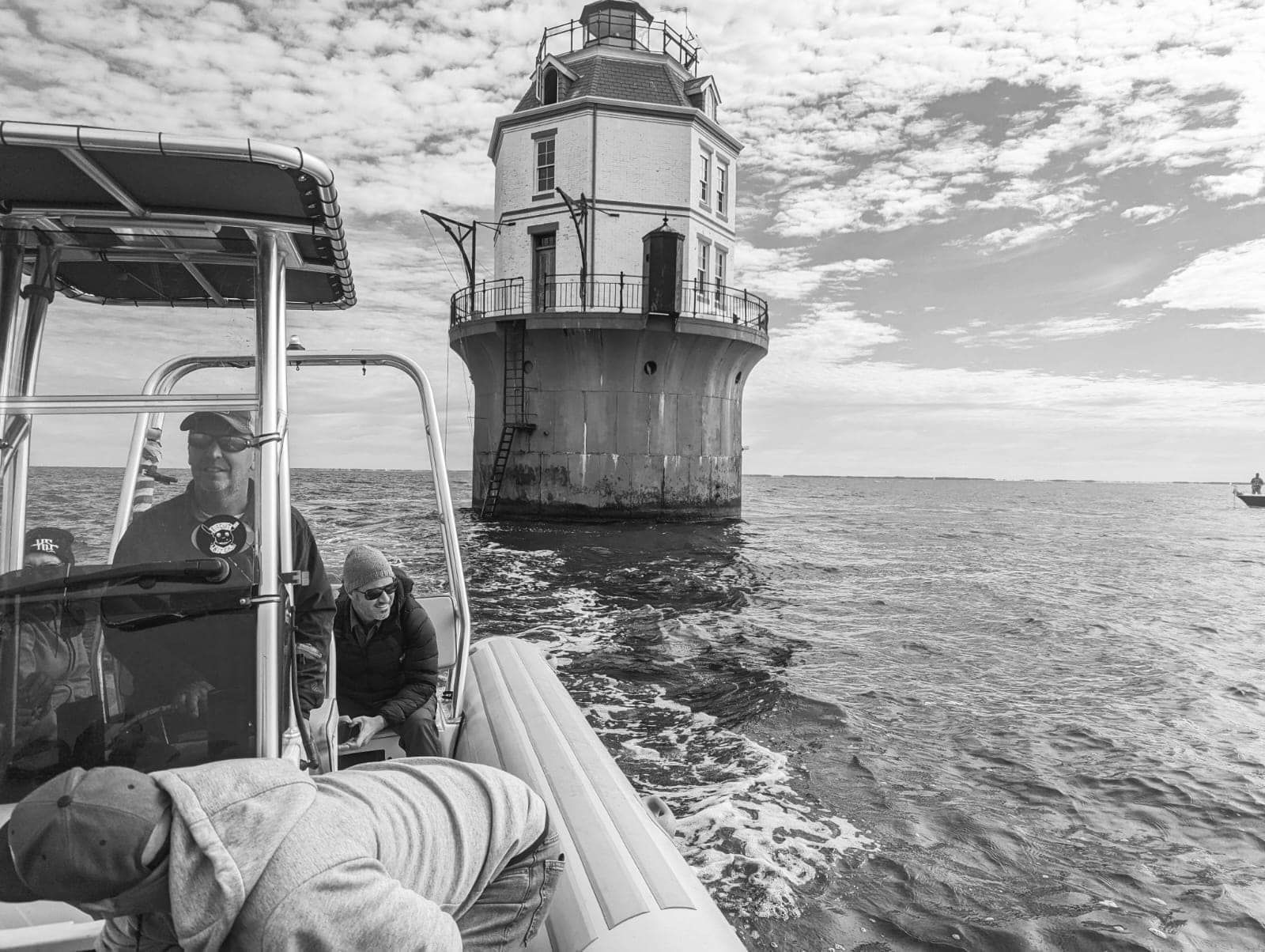 black and white photo of motorboat with the lighthouse in the background