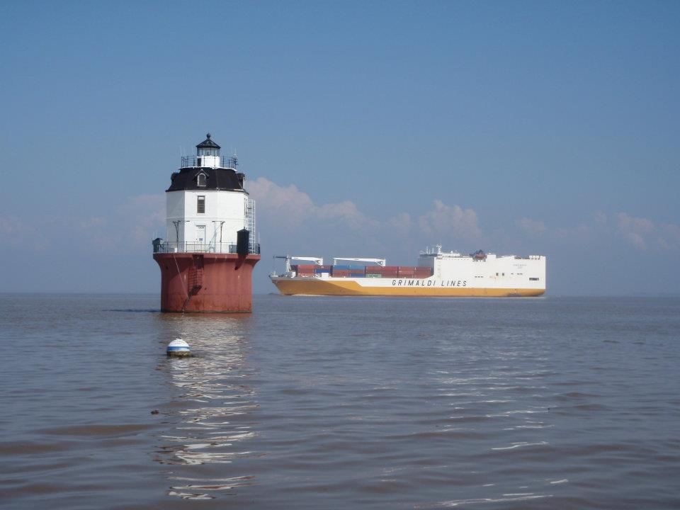 container cargo ship sails behind the lighthouse