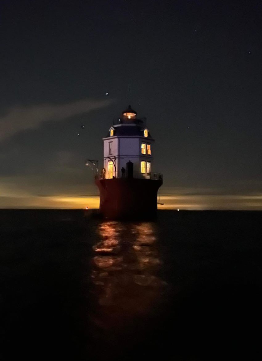 the Baltimore Lighthouse at night with windows glowing yellow from lights inside