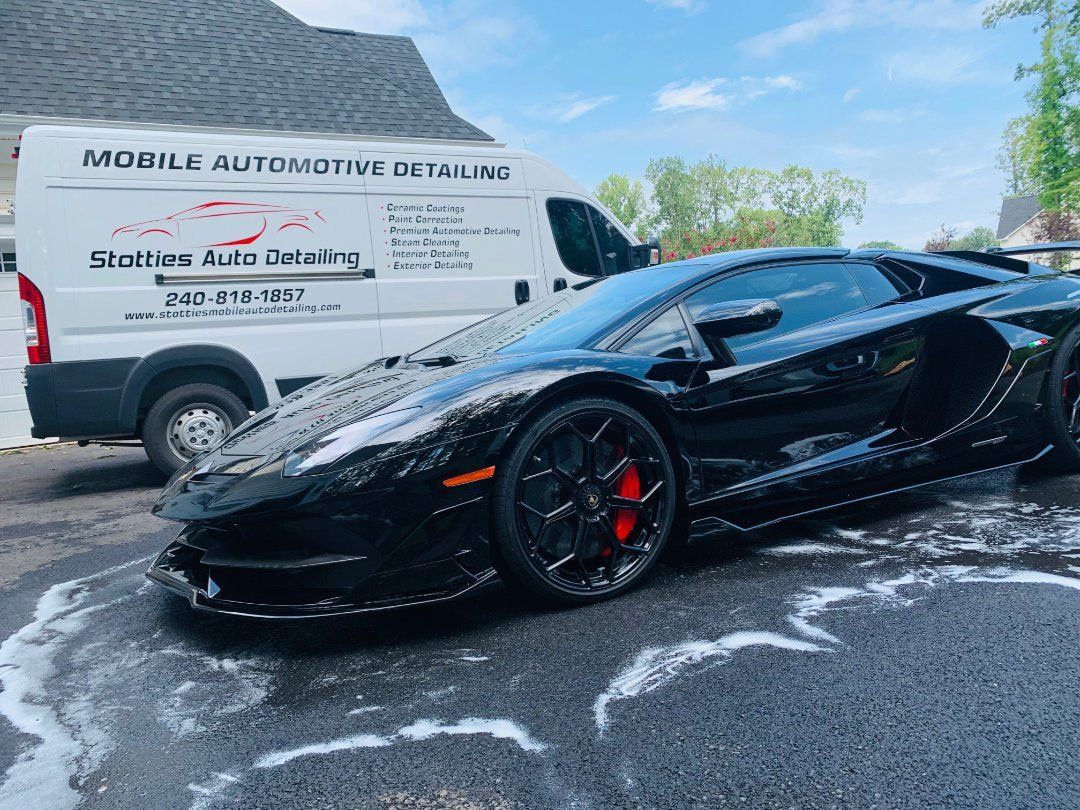 Black Lamborghini being washed, parked next to a white service van.