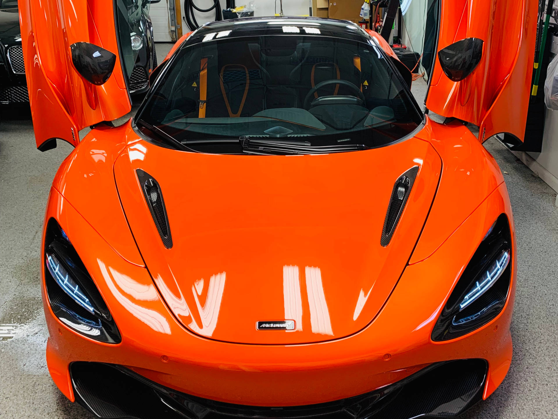 Bright orange McLaren sports car with doors open.
