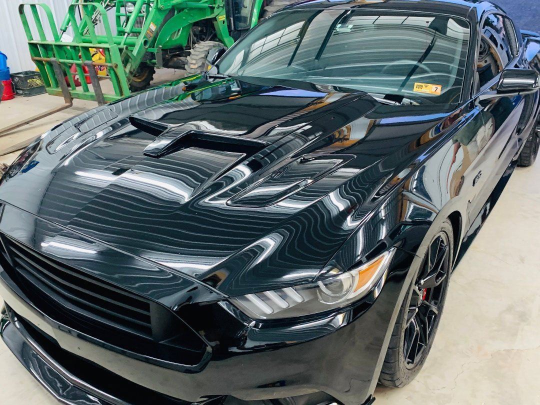 Black Ford Mustang with hood scoop, parked indoors near green equipment.