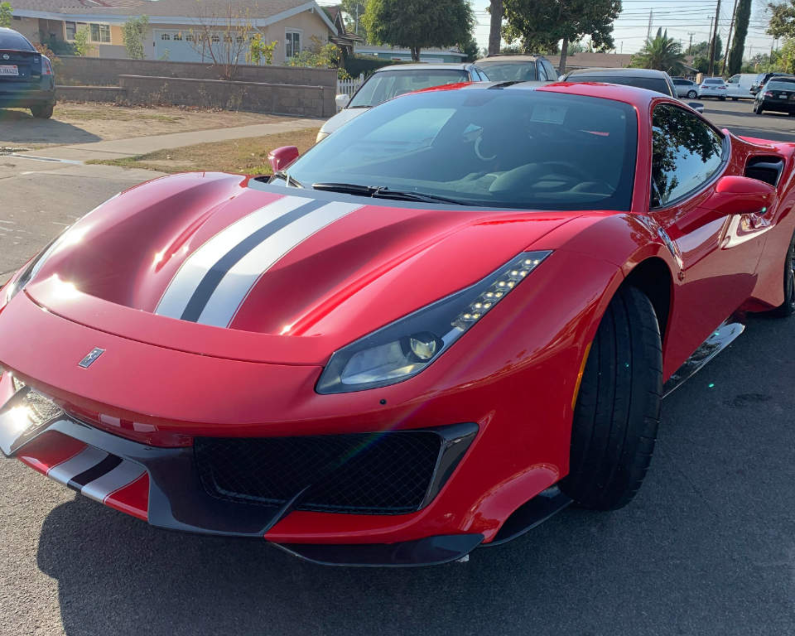 Red Ferrari sports car with white racing stripes parked on a street in front of houses.