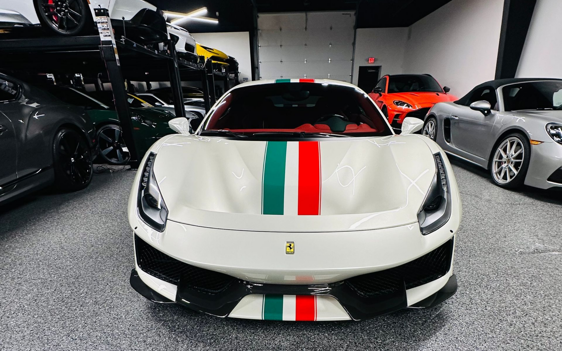 White Ferrari with green and red racing stripes in a showroom with other luxury cars.