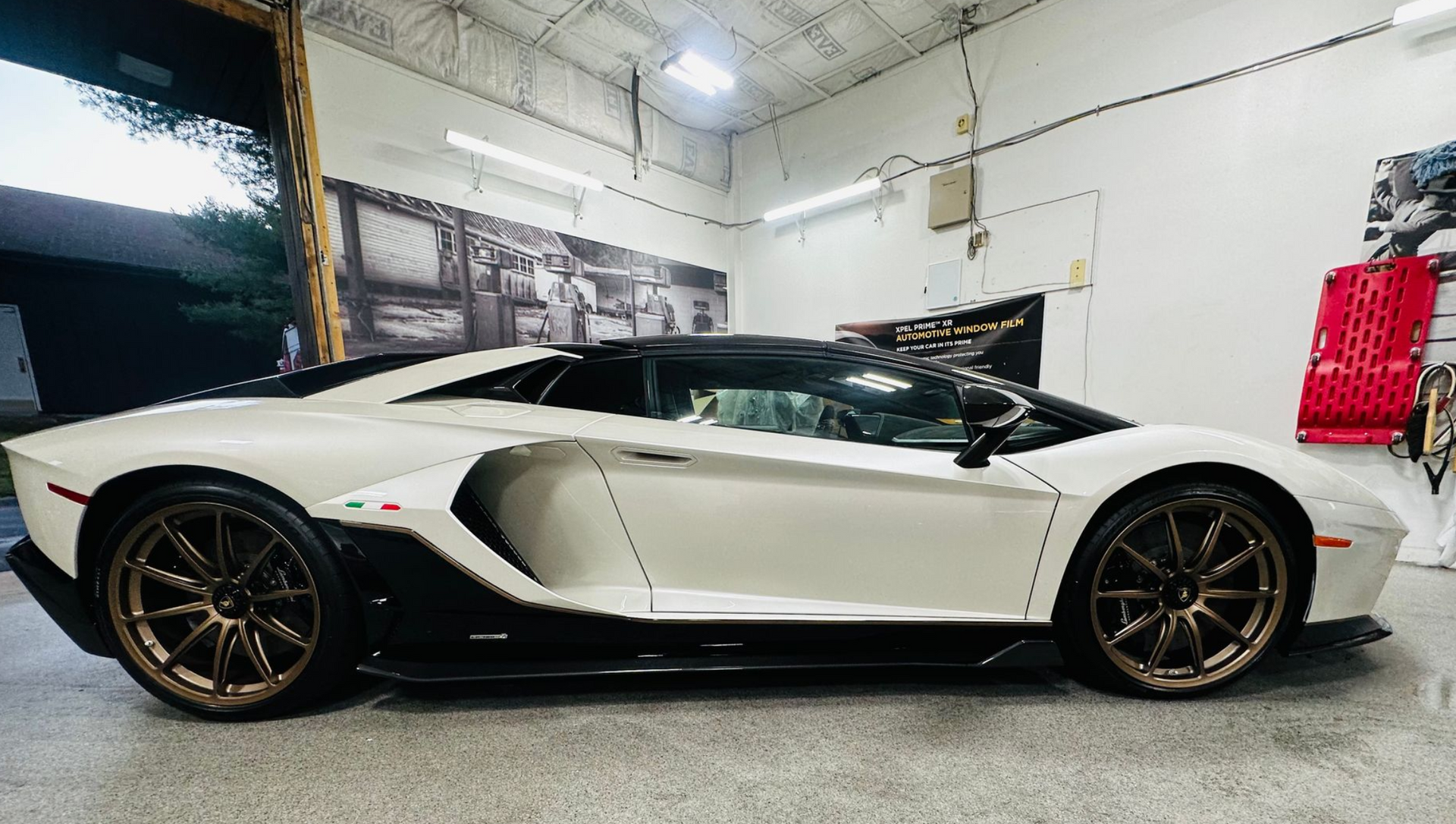 White and black Lamborghini Aventador in a garage, with bronze wheels.