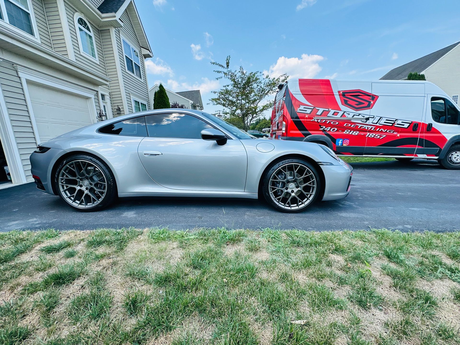 A dark blue McLaren parked on asphalt next to a red and white branded service van in a grassy outdoor area.