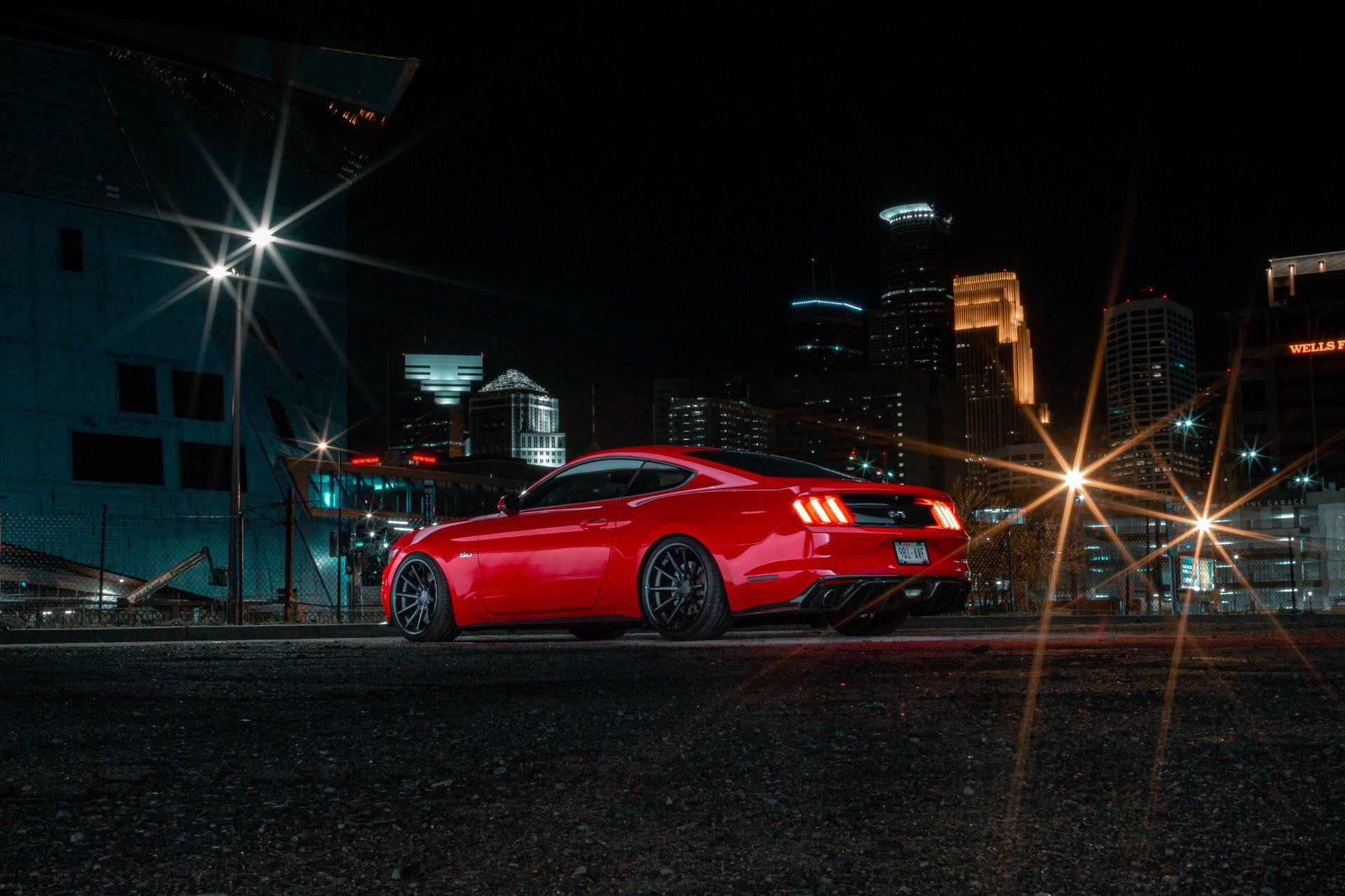 Red sports car parked on a dark street at night, city skyline in the background.