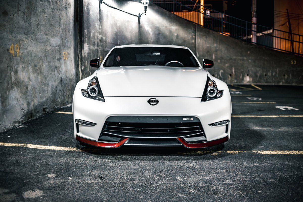 White Nissan 370Z sports car parked in a dark, concrete parking garage, with red accents.