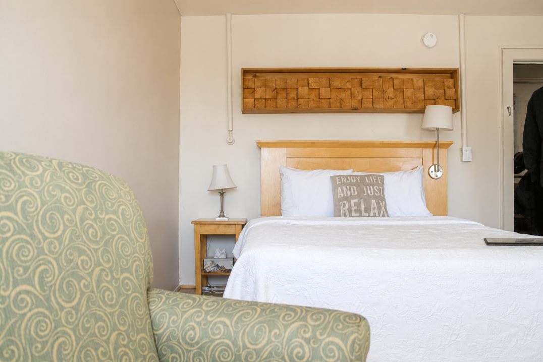 Hotel room with two beds, green chairs, exposed wooden beam, and window with curtains