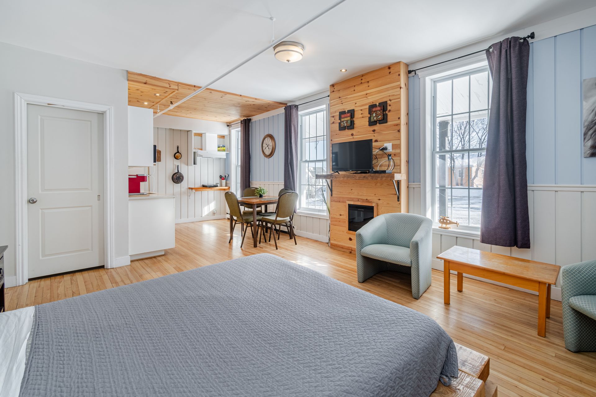 Bright bedroom with a bed, red floral art, large windows, and wooden floors