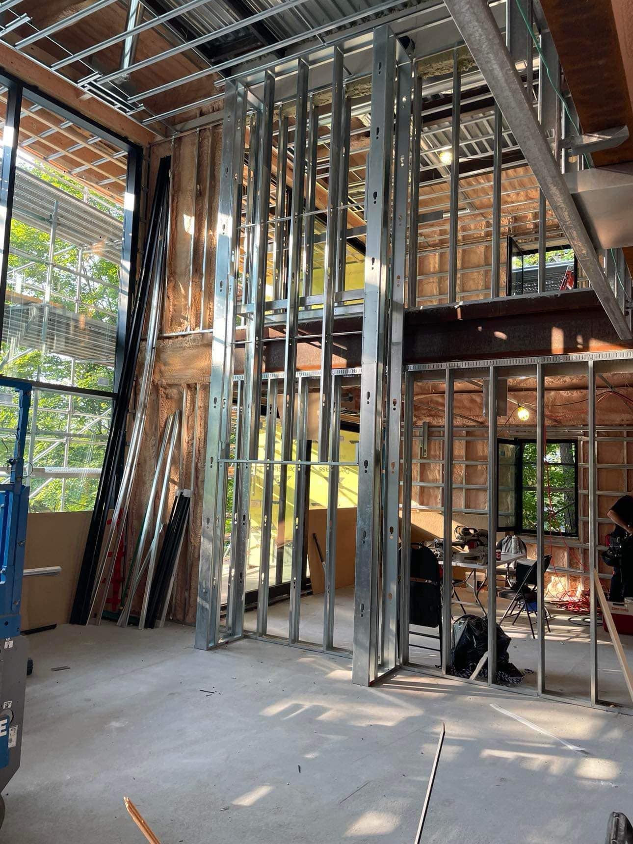 Un chantier de construction montrant une ossature métallique, de grandes fenêtres et une mezzanine en cours d'aménagement.