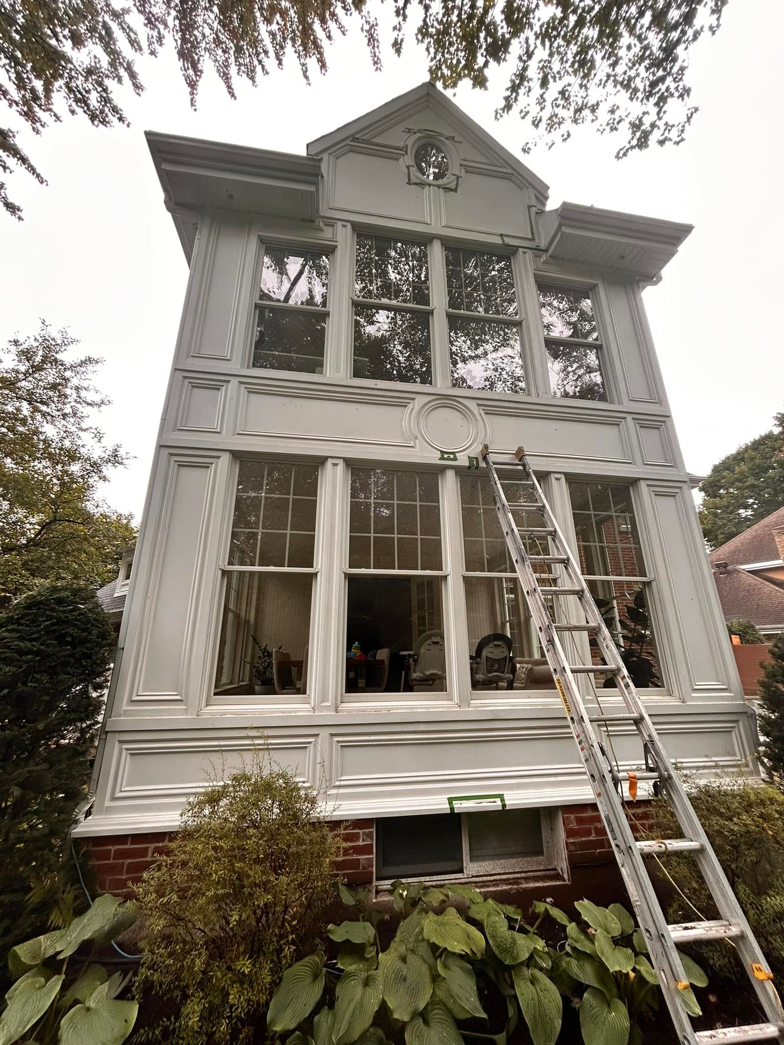 Une maison à l'extérieur peinte en argent, avec de grandes baies vitrées et une haute échelle métallique appuyée contre elle.