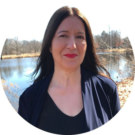 A woman is standing in front of a lake and smiling.