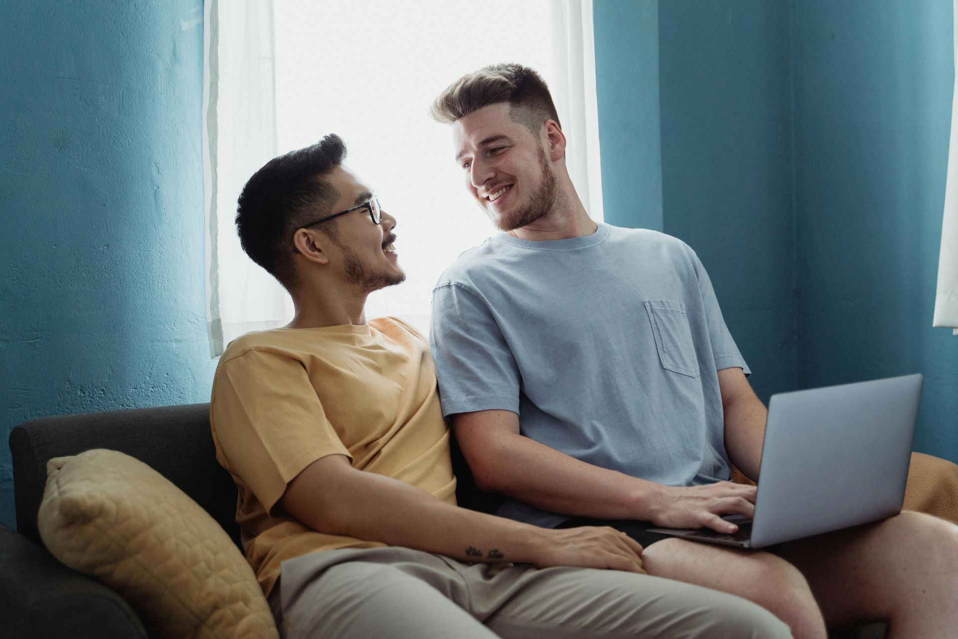 Two men are sitting on a couch with a laptop.