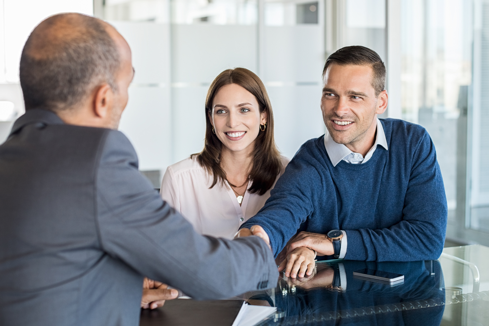 A man and a woman are shaking hands with a man while sitting at a table.