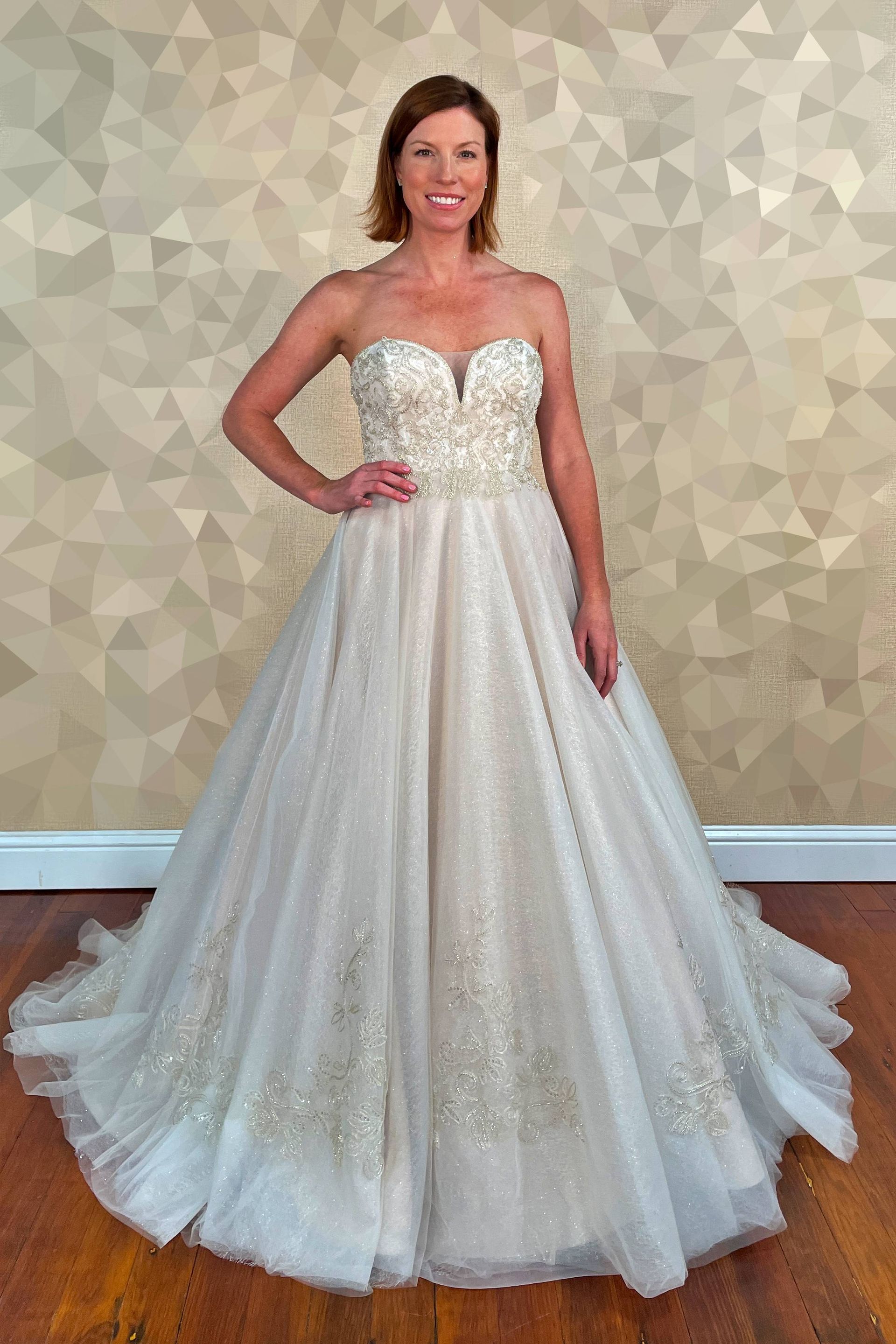 Woman in a beaded strapless gown, standing with hand on hip. Beige and gold tones.