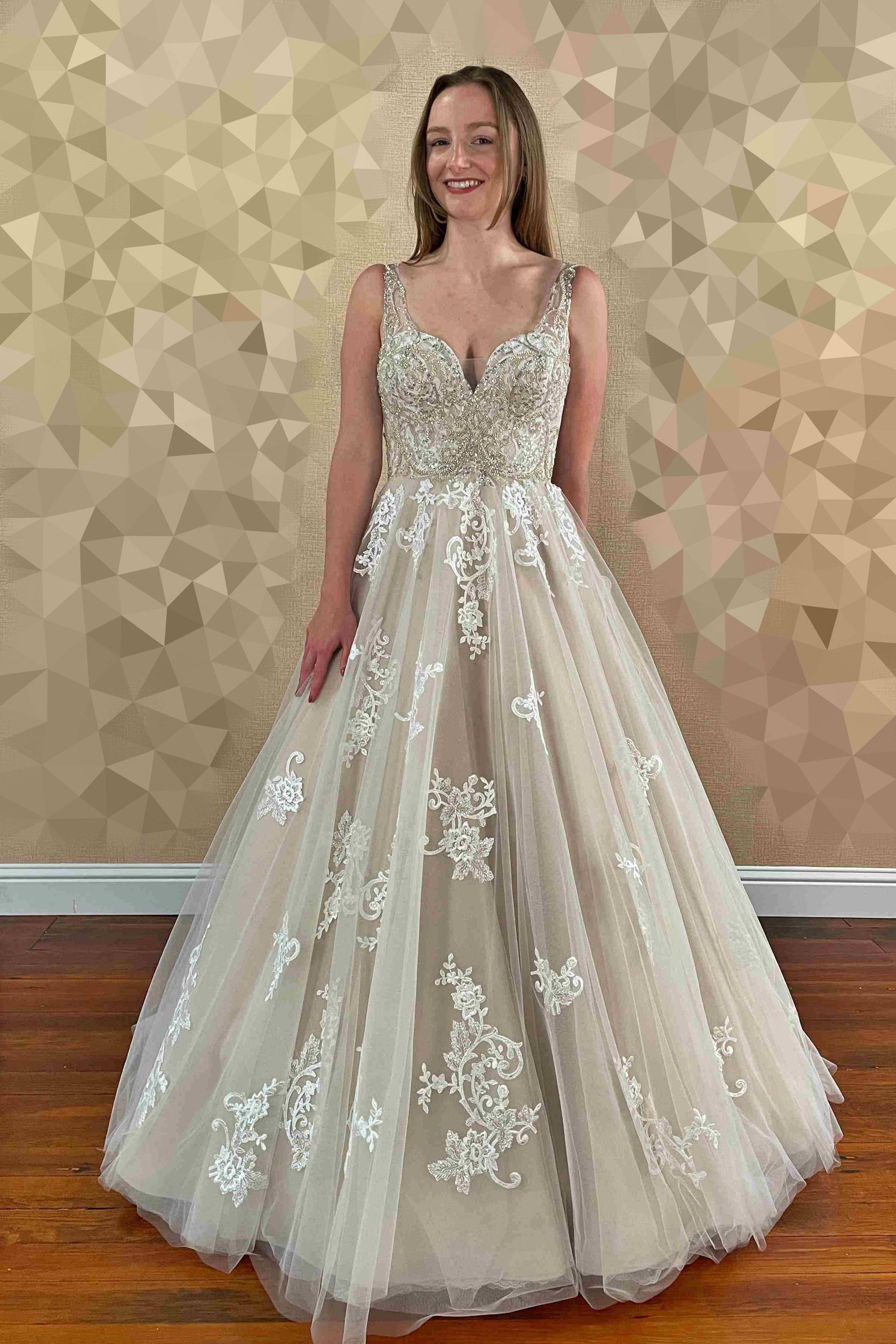 Woman in a formal gown with floral details, standing in front of a patterned wall.