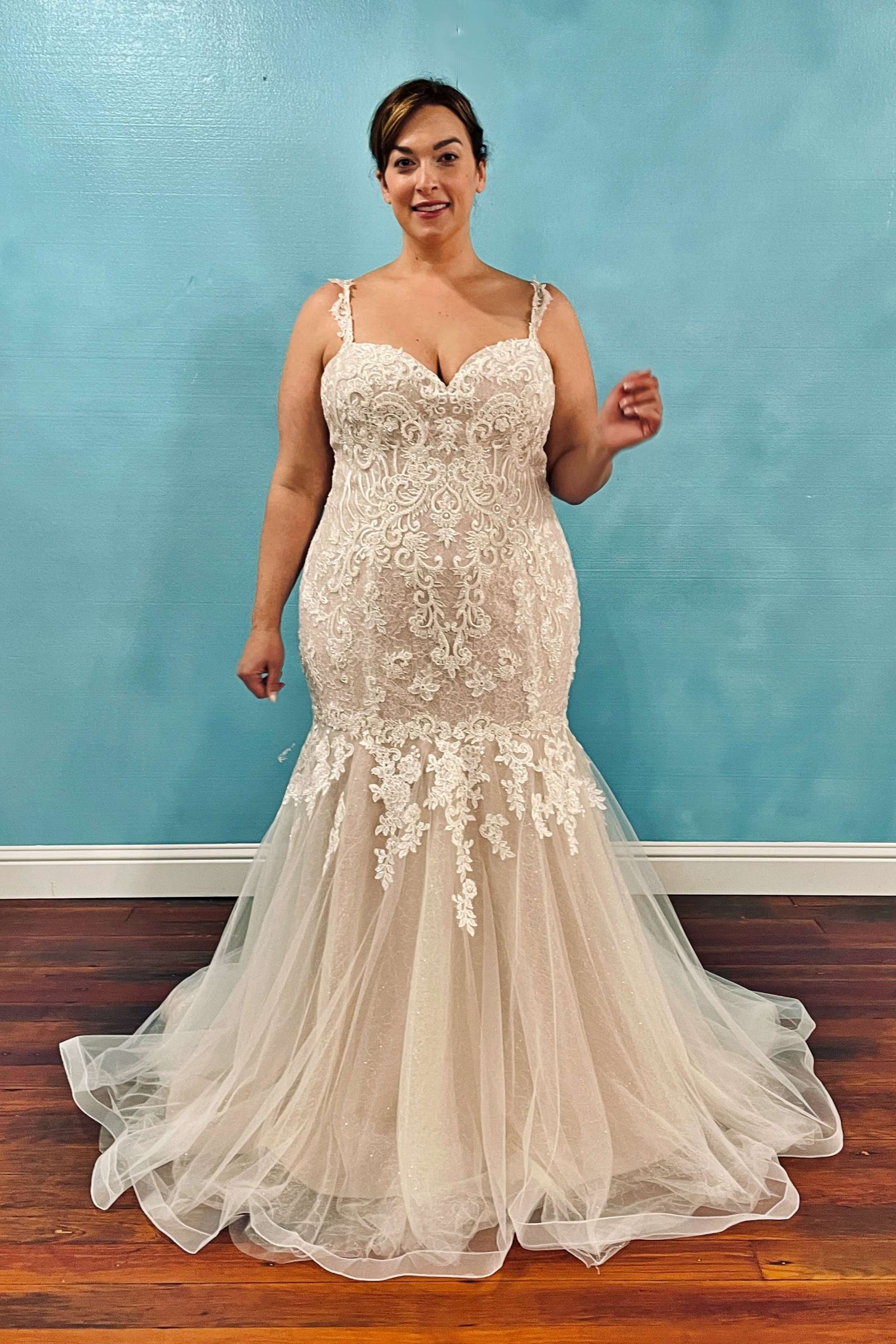 Woman in a white lace wedding dress with a mermaid silhouette, standing in front of a blue wall.