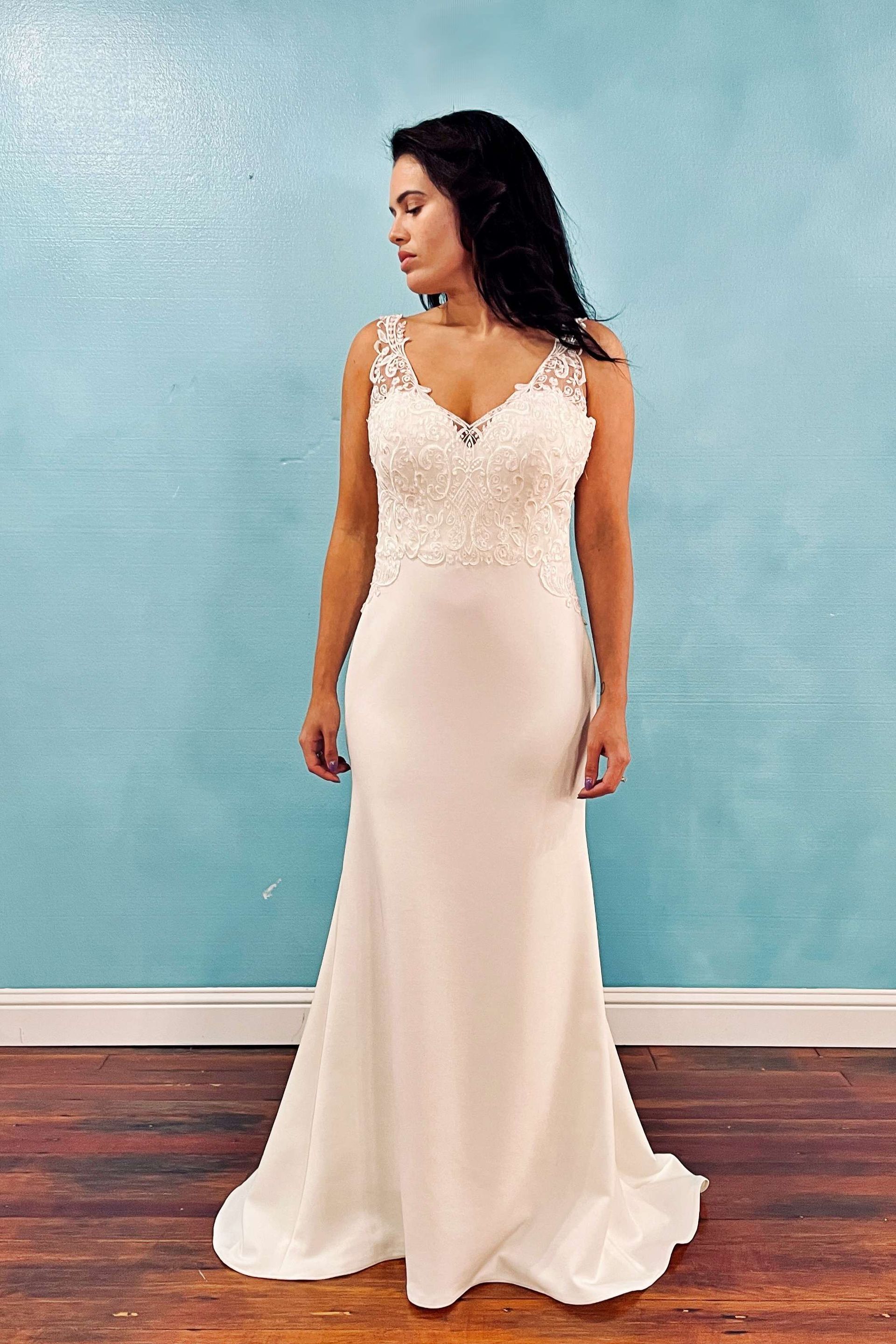 Woman in a white wedding dress stands in front of a blue wall.