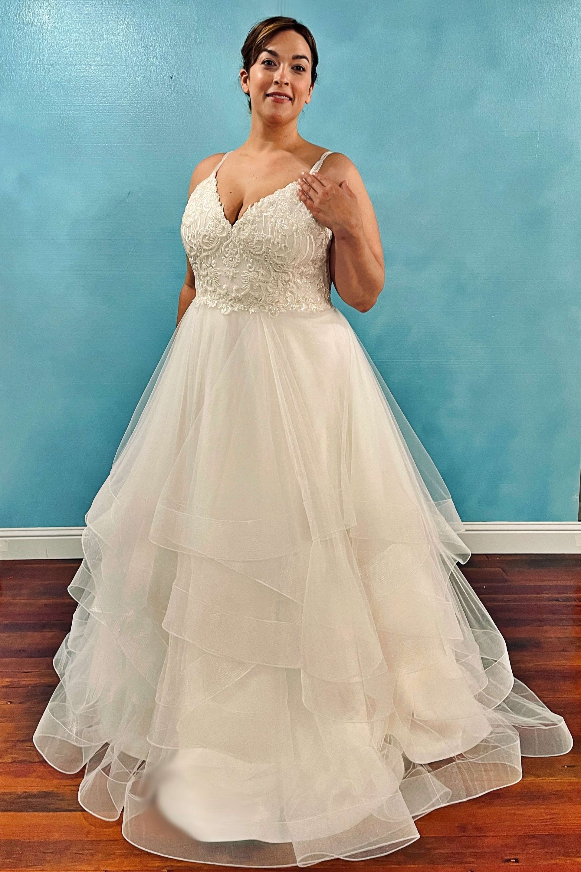 Woman in a white wedding dress with beading on the bodice, standing against a teal wall.