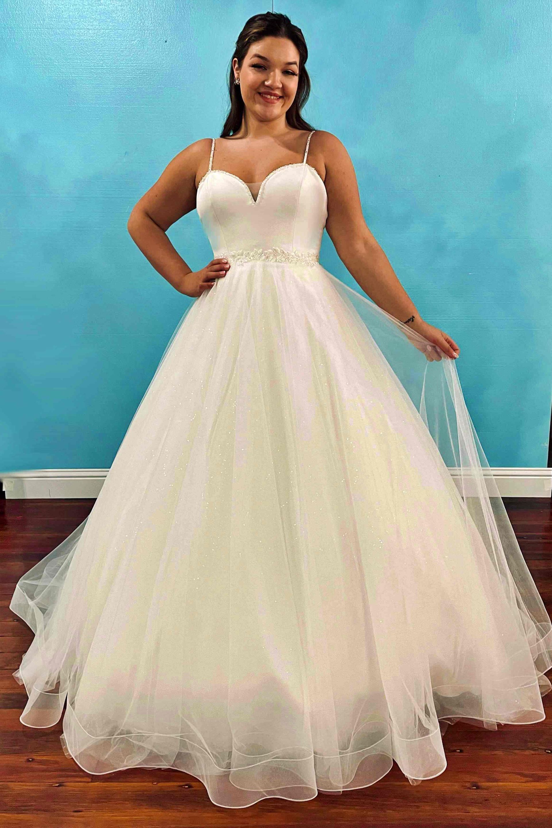 Woman in a white wedding gown, smiling, in front of a blue wall.