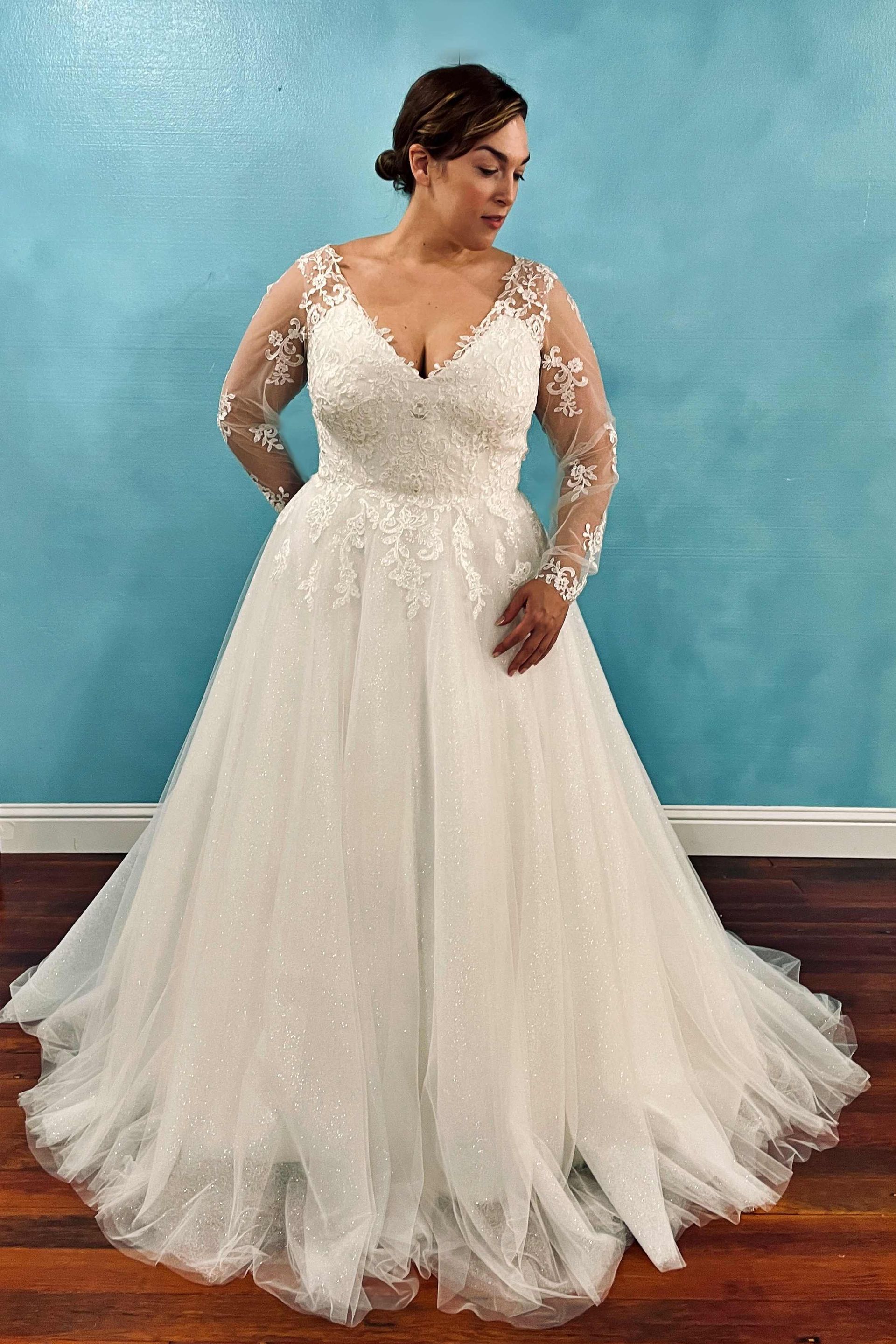 Woman in a white wedding gown, looking down, posing in front of a blue wall and wooden floor.