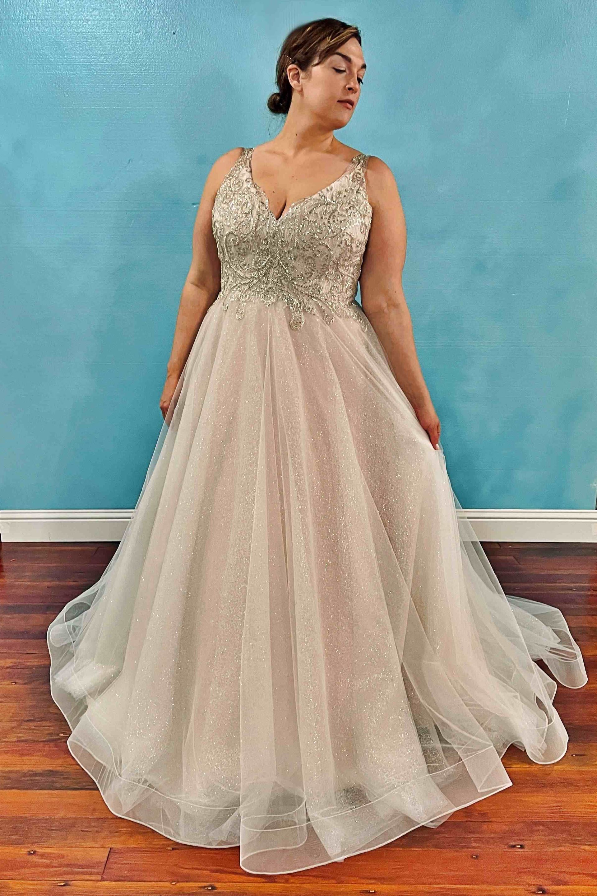 Woman in a sparkly wedding dress with a beaded bodice, standing in front of a blue wall.