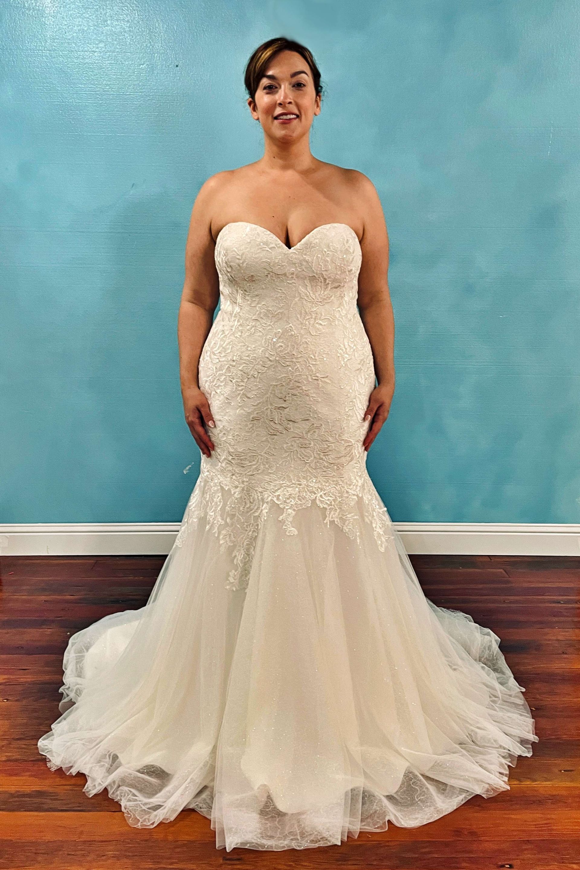 Woman in a strapless ivory mermaid wedding dress, standing in front of a blue wall.