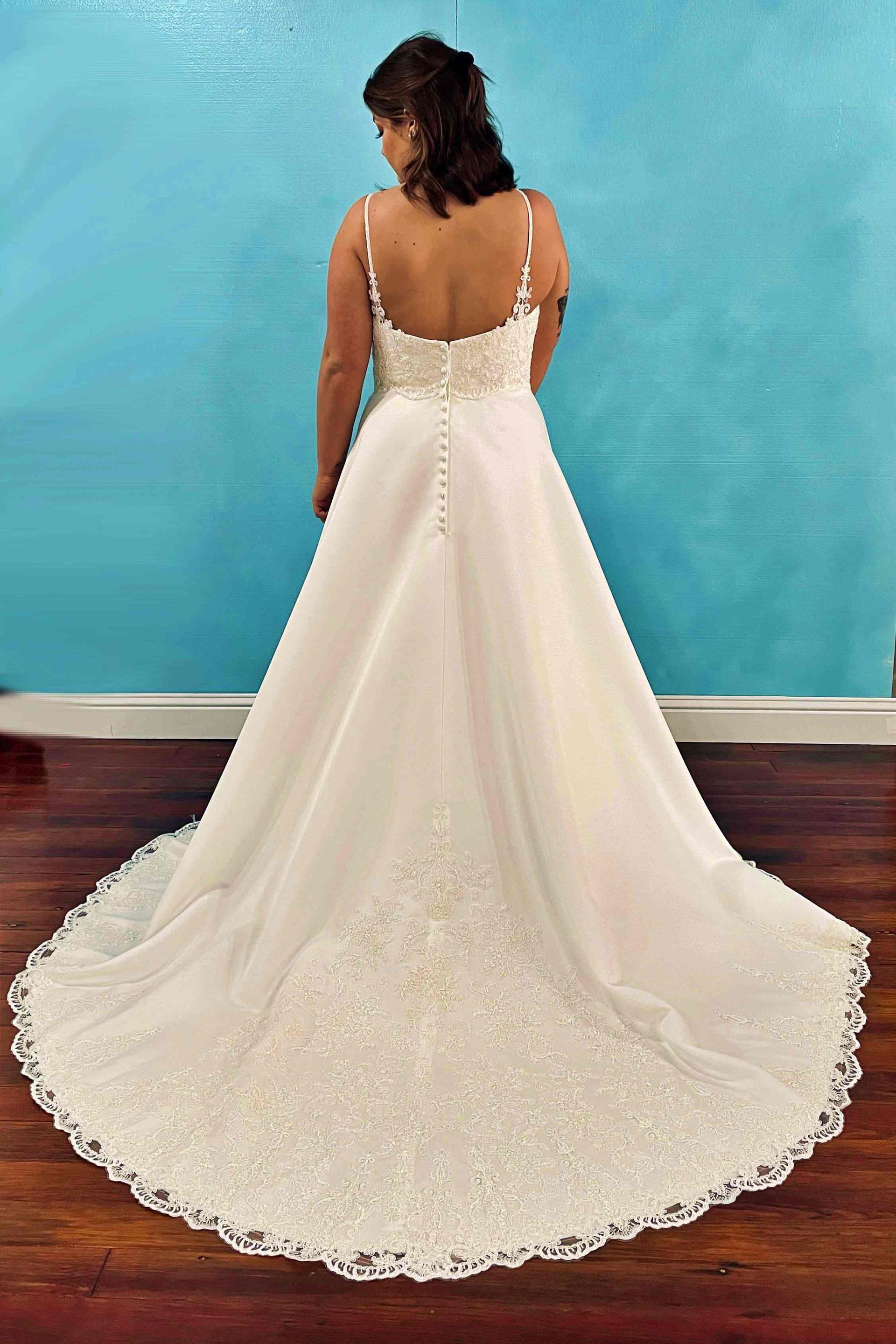 Woman in white wedding dress, back view, standing in front of a blue wall.