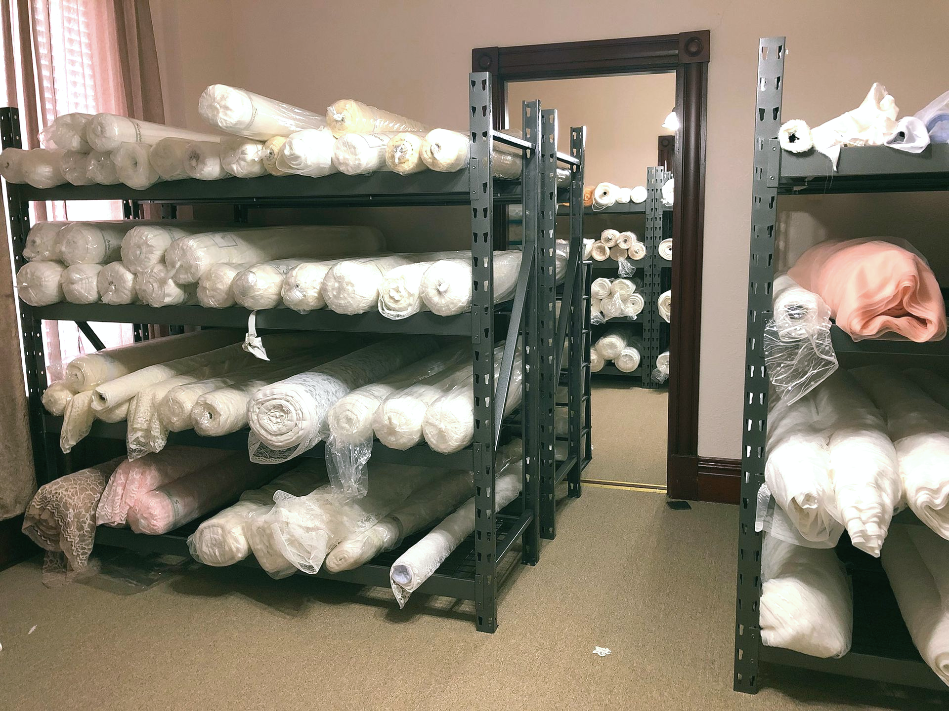 Shelves filled with rolled fabric bolts in a room; mirror reflects more fabric rolls.