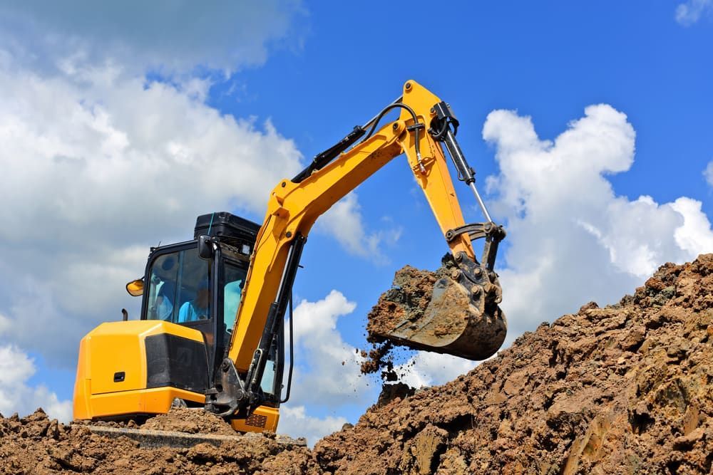 Yellow Excavator Digging in a Pile of Dirt Against a Blue Sky — Rhino Excavator & Bobcat Hire in Holloways Beach, QLD