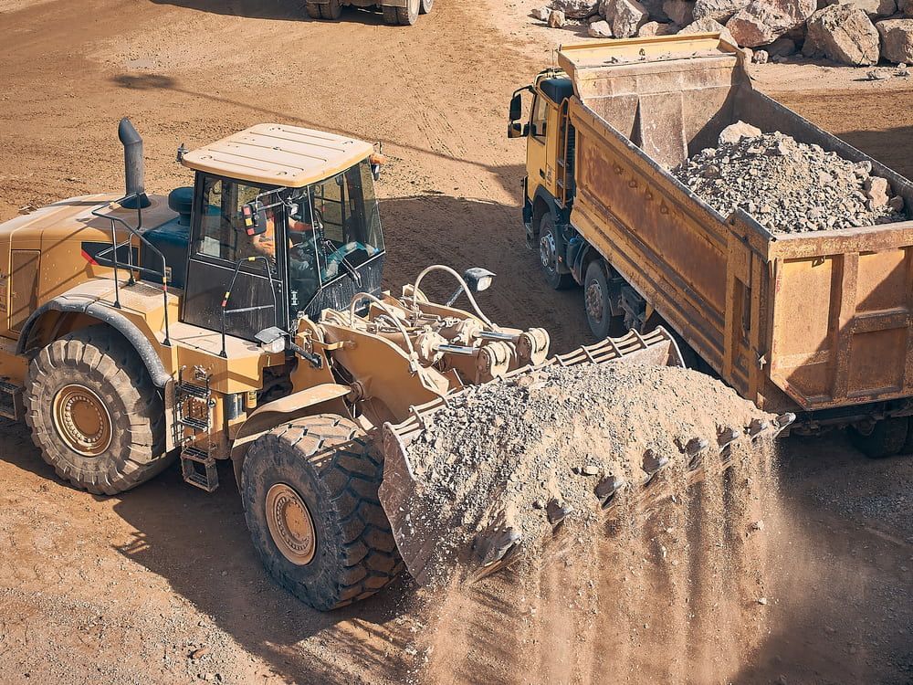 Yellow Loader Dumping Rocks Into a Dump Truck at a Construction Site — Rhino Excavator & Bobcat Hire in Holloways Beach, QLD