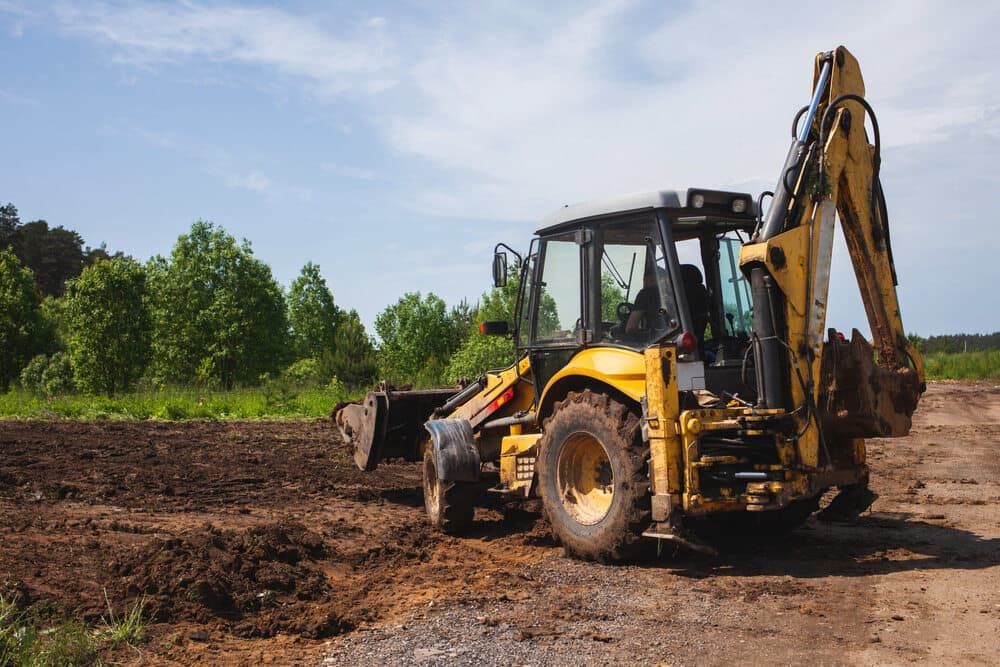 Yellow Backhoe on a Dirt Field With a Blue Sky and Trees in the Background — Rhino Excavator & Bobcat Hire in Redlynch, QLD 