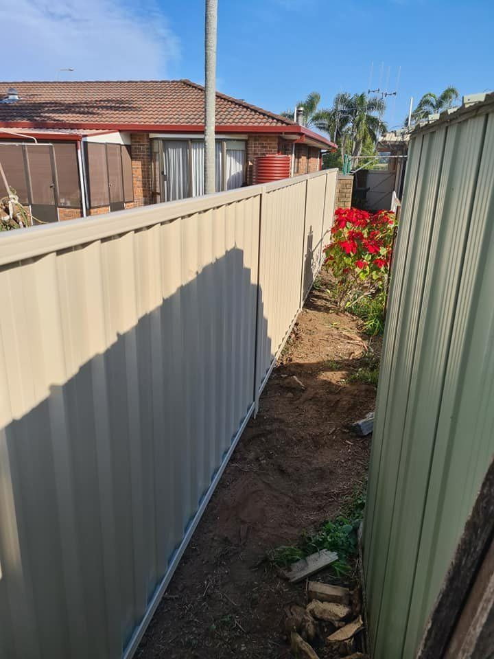 A Fence Surrounds a Garden with Flowers and A House in The Background — D & B Fencing in Taree, NSW