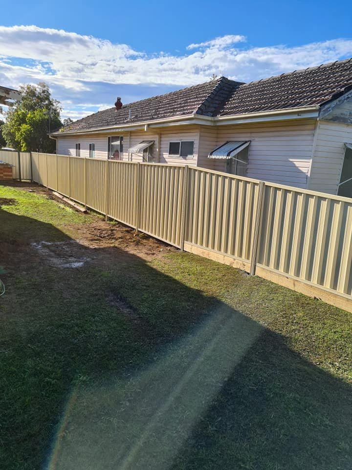 A White Fence Is Surrounding a House on A Sunny Day — D & B Fencing in Taree, NSW
