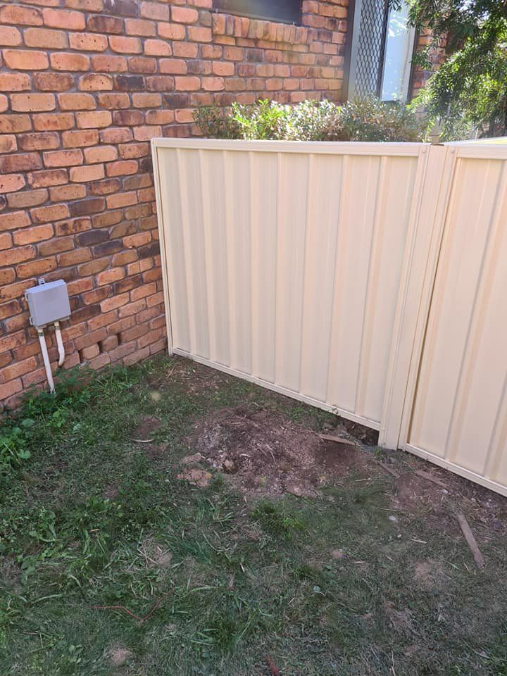 A White Fence Is Sitting in Front of A Brick Wall — D & B Fencing in Taree, NSW