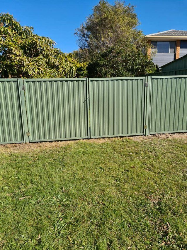 A Green Fence with A Gate Is in The Middle of A Lush Green Field — D & B Fencing in Nabiac, NSW