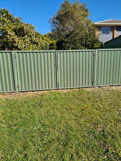 A Green Fence with A Gate Is in The Middle of A Lush Green Field — D & B Fencing in Taree, NSW