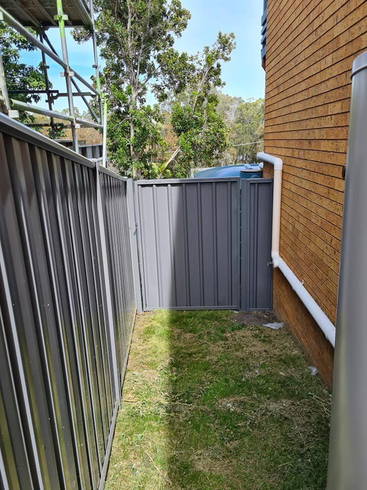 A Fence Is Surrounding a Grassy Area Next to A Brick Building — D & B Fencing in Wingham, NSW