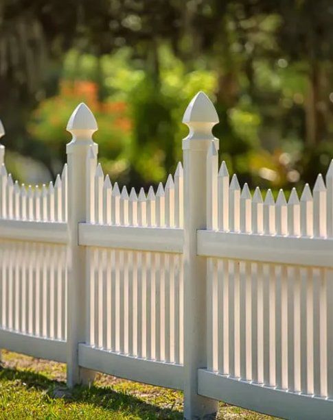 A White Picket Fence Is Sitting on Top of A Lush Green Field — D & B Fencing in Taree, NSW