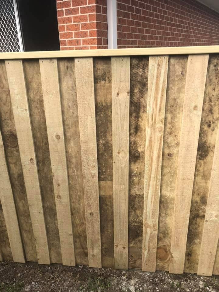 A Wooden Fence Is Sitting in Front of A Brick Building — D & B Fencing in Taree, NSW