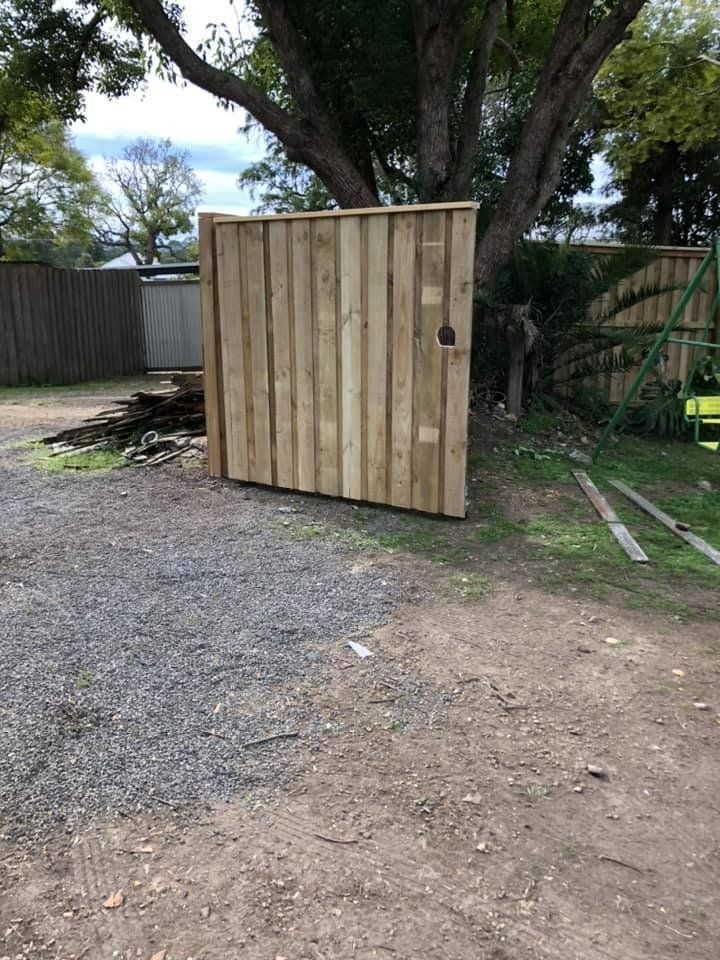 A wooden gate is sitting in the middle of a dirt road next to a tree.