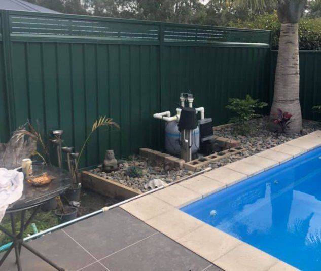 A Swimming Pool with A Green Fence Surrounding It — D & B Fencing in Taree, NSW