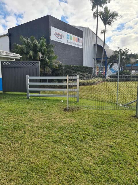 There Is a Fence in The Grass in Front of A Building — D & B Fencing in Taree, NSW