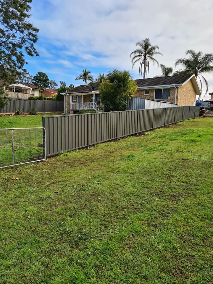 A Fence Surrounds a Lush Green Field with A House in The Background — D & B Fencing in Harrington, NSW